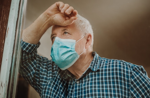 Foto hombre mayor en cuarentena por coronavirus, covid-2019 en una casa, mirando hacia afuera por la ventana