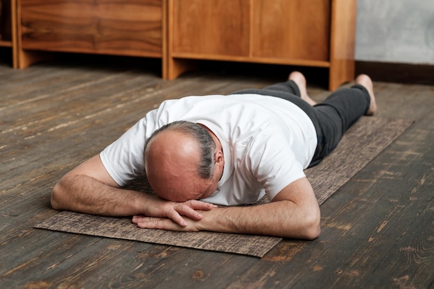 Hombre mayor descansando después de hacer ejercicio de yoga en el suelo Deportes en casa para la salud