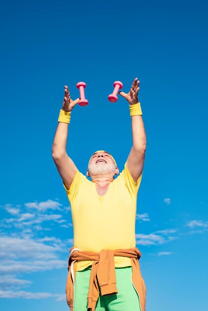 El hombre mayor disfruta de un estilo de vida deportivo Cuidado del cuerpo y atención médica Hombre mayor haciendo ejercicio en el cielo azul Viejo hombre maduro haciendo ejercicio con pesas