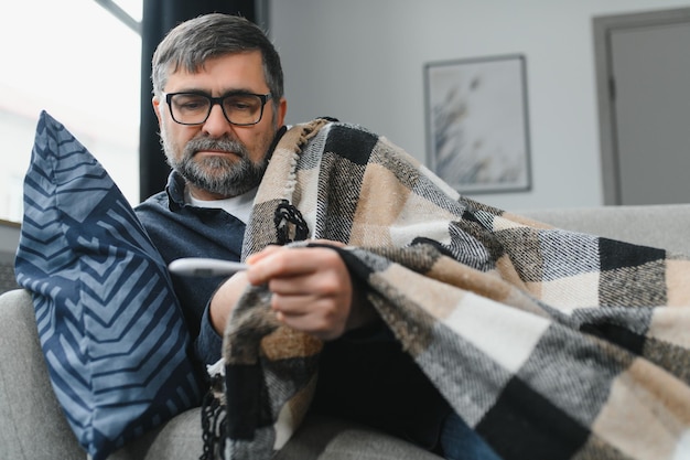 Hombre mayor enfermo usando un termómetro comprobando su temperatura sufriendo de gripe estacional o resfriado