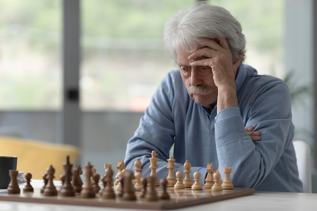 Hombre mayor enfocado jugando al ajedrez está mirando el tablero de ajedrez y pensando