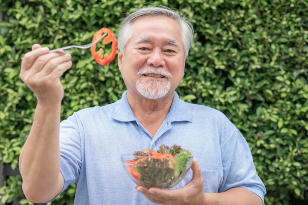 El hombre mayor de estilo de vida se siente feliz disfruta comiendo ensalada fresca de comida dietética sobre fondo de naturaleza de planta verde