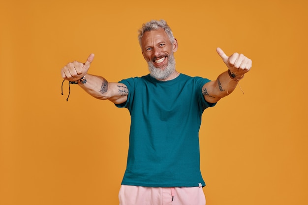 Hombre mayor feliz mostrando sus pulgares hacia arriba mientras está de pie contra el fondo naranja