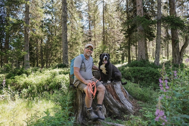 Hombre mayor feliz que tiene un descanso con el perro durante el día de trekking en el bosque de montaña