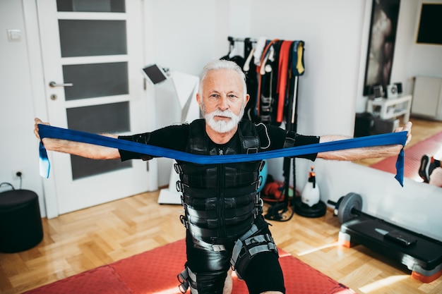 Hombre mayor guapo y positivo haciendo ejercicios en traje de estimulación muscular eléctrica.