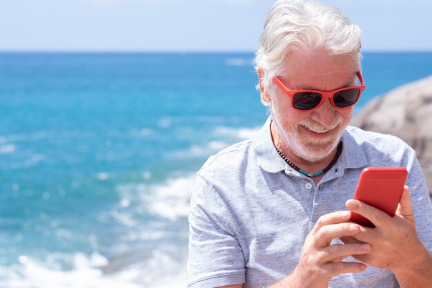 Hombre mayor hermoso despreocupado que usa el teléfono móvil en el mar Jubilación feliz Estilos de vida alegres