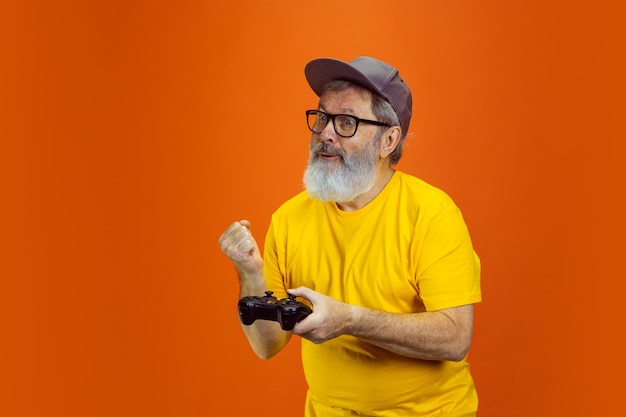 Hombre mayor hipster usando dispositivos gadgets en tecnología de fondo naranja y alegre estilo de vida de ancianos