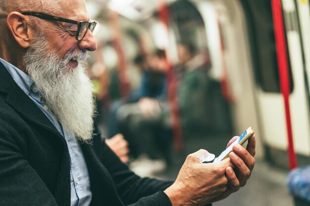 Hombre mayor hipster usando un teléfono inteligente en el metro Centrándose en las manos sosteniendo el teléfono móvil