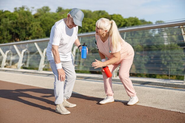 El hombre mayor se lesionó la rodilla al correr y su esposa preocupada se encuentra cerca en la pasarela