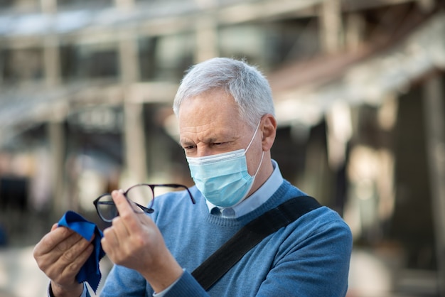 Hombre mayor limpiando sus anteojos empañados debido a la máscara, concepto de visión de coronavirus covid