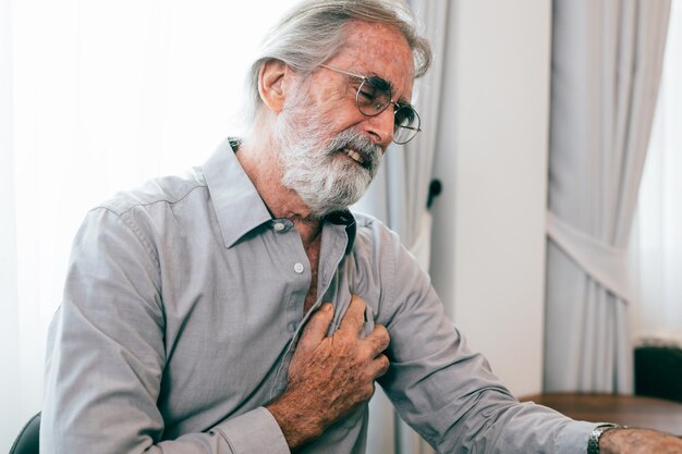 Hombre mayor con la mano en el pecho y que sufre de problemas cardíacos en casa