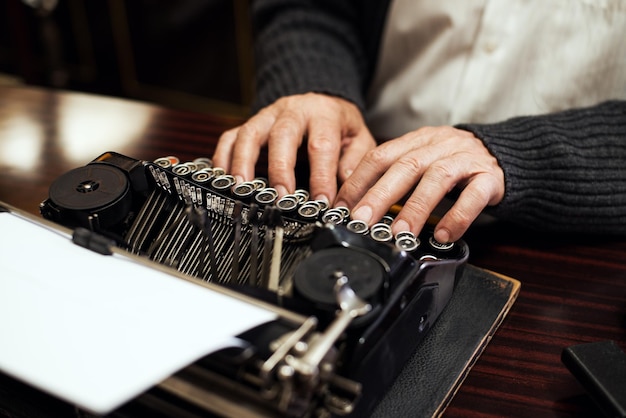 Hombre mayor manos escribiendo en máquina de escribir obsoleta.