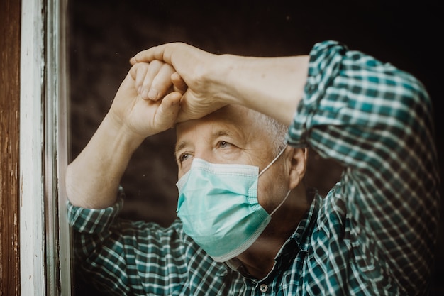Hombre mayor con máscara médica en el hogar durante el coronavirus, pandemia covid-2019, quédese en casa