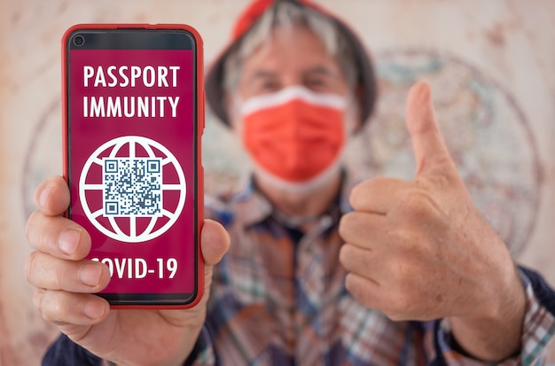 Hombre mayor con mascarilla muestra la aplicación de pasaporte de salud para personas vacunadas contra el coronavirus