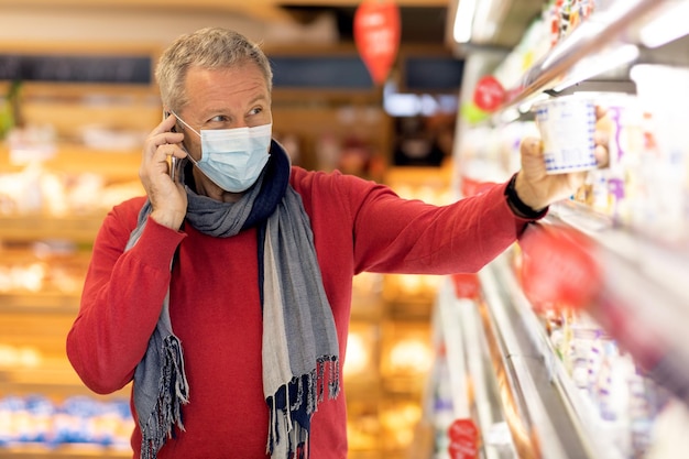 Hombre mayor con mascarilla que tiene una conversación telefónica mientras compra