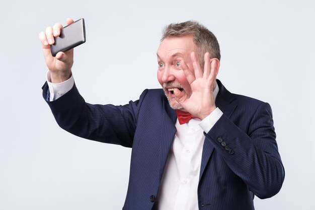 Hombre mayor mirando la pantalla del teléfono inteligente saludando como si tuviera video chat