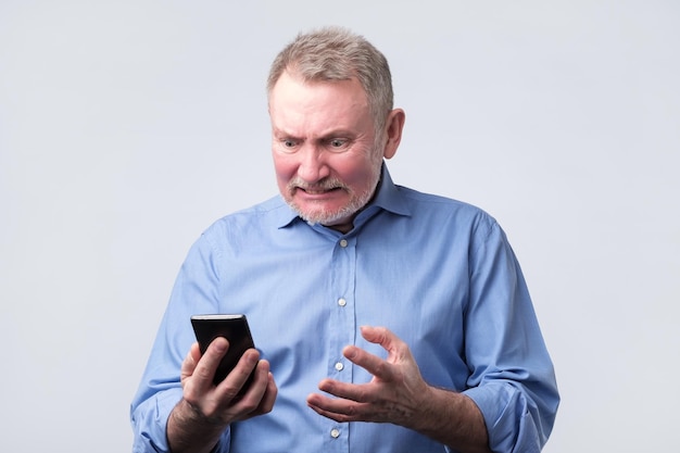 Hombre mayor molesto con camisa azul mirando el teléfono móvil