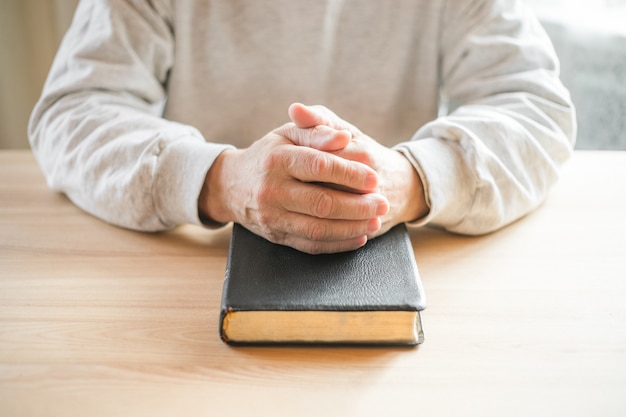 Hombre mayor orando, leyendo una vieja Biblia en sus manos.