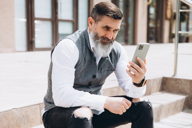 Un hombre mayor de pelo gris barbudo usa y habla en un teléfono inteligente