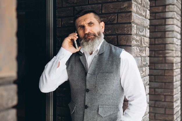 Un hombre mayor de pelo gris barbudo usa y habla en un teléfono inteligente
