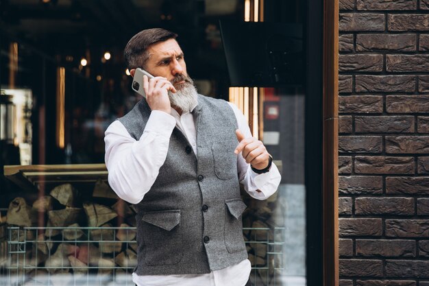 Un hombre mayor de pelo gris barbudo usa y habla en un teléfono inteligente