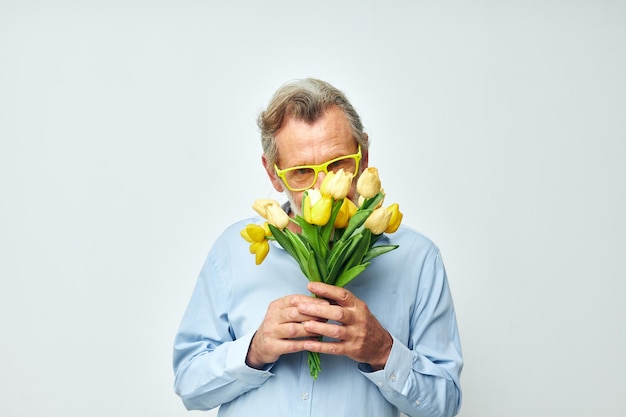 Hombre mayor de pelo gris con una camisa azul con un ramo de flores de fondo claro