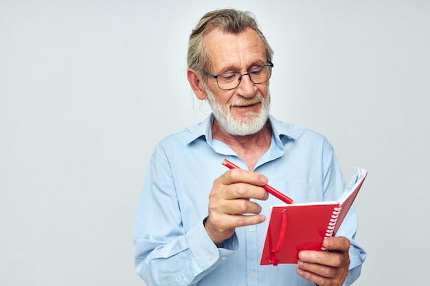Hombre mayor de pelo gris con cuaderno rojo y fondo claro de pluma