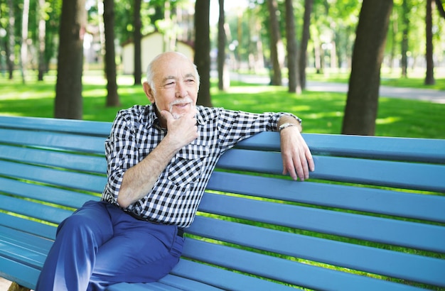 Hombre mayor pensativo al aire libre. Anciano en casual sentado en el banco en el parque soleado, espacio de copia