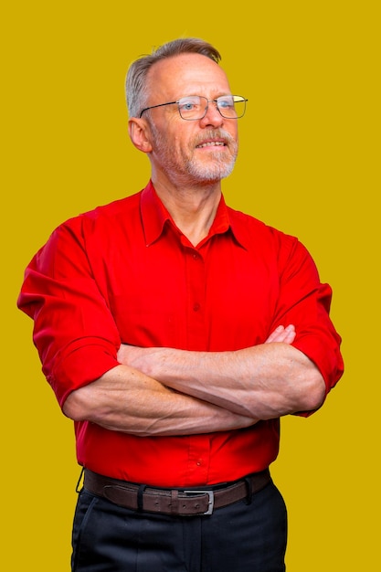 Foto hombre mayor está de pie con las manos cruzadas aisladas sobre fondo amarillo camisa roja hombre con gafas