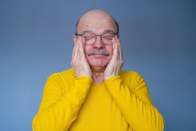 Hombre mayor preocupado con gafas frotándose los ojos cansados. foto de estudio