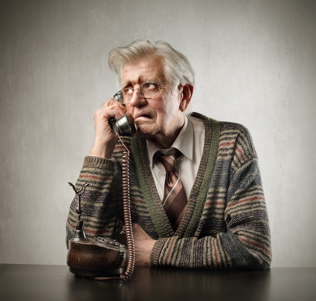 Hombre mayor preocupado que habla en un teléfono clásico