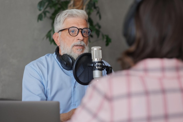 Un hombre mayor y una presentadora en un estudio de grabación crean una presentadora de radio o entrevistadora de podcast