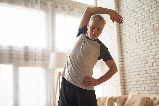 Hombre mayor que estira entrenamiento fácil en casa.