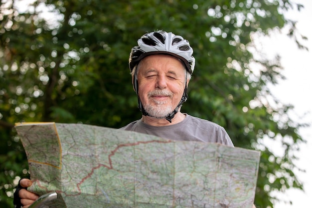 Hombre mayor que mira el mapa durante su viaje en bicicleta o en bicicleta en el concepto de estilo de vida saludable del bosque
