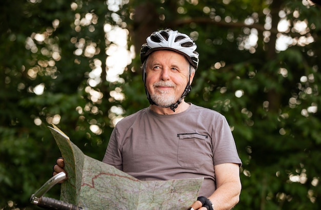Hombre mayor que mira el mapa durante su viaje en bicicleta o en bicicleta en el concepto de estilo de vida saludable del bosque