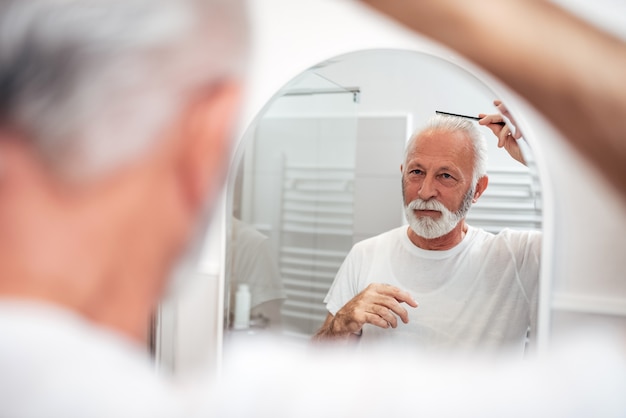 Hombre mayor que peina su pelo en el cuarto de baño.