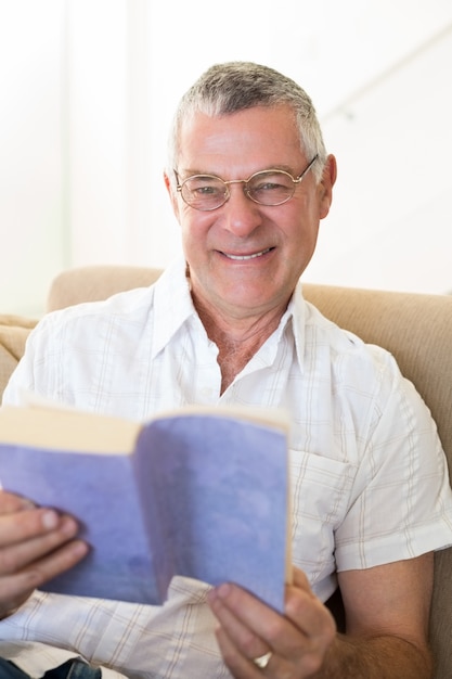 Hombre mayor que sostiene el libro en el sofá