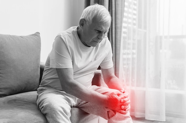 Hombre mayor que sufre de dolor en la rodilla en casa. Concepto de problemas con las articulaciones como la artritis.