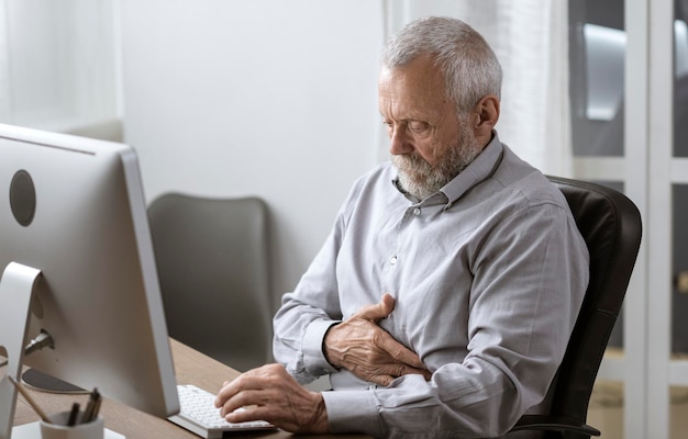 Foto hombre mayor que trabaja en la oficina y tiene un mal dolor de estómago anciano y concepto de salud