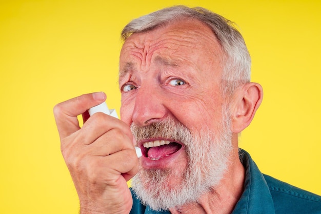 Hombre mayor que usa un inhalador para el asma en el fondo amarillo del estudio.