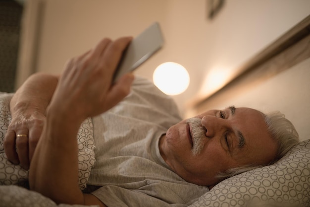 Hombre mayor que usa un teléfono inteligente mientras se acuesta en la cama por la noche