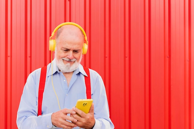 Hombre mayor que usa un teléfono inteligente móvil mientras escucha una lista de reproducción de música con auriculares Estilo de vida de personas mayores y concepto tecnológico