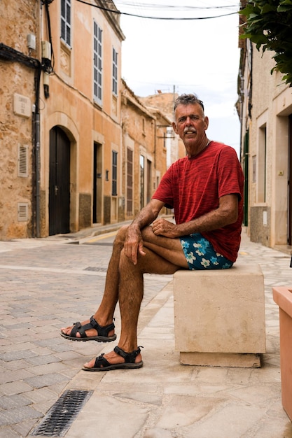 Un hombre mayor que viaja sentado mirando la cámara en un pintoresco pueblo de España