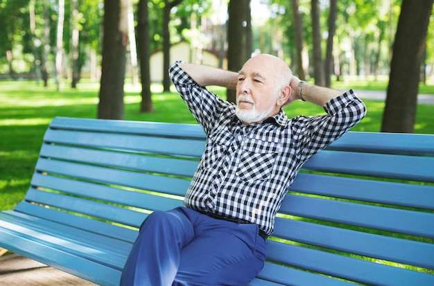 Hombre mayor relajado en casual al aire libre. Anciano sentado en el banco en el parque, espacio de copia