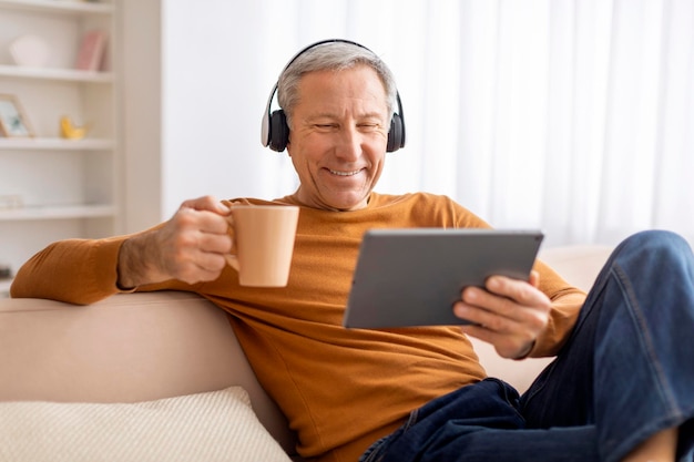 Hombre mayor relajado chillando en casa usando tableta y auriculares