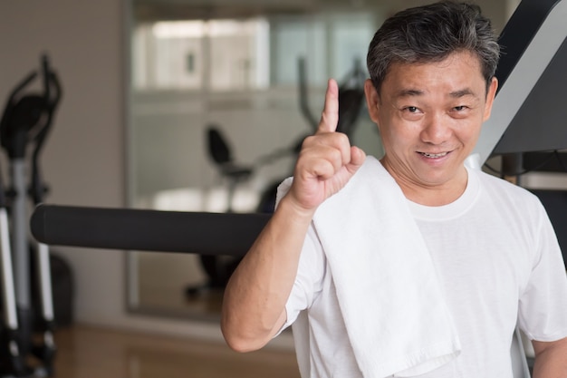 Hombre mayor sano y feliz que trabaja en el gimnasio, dando el gesto del dedo n. ° 1, concepto ganador o éxito