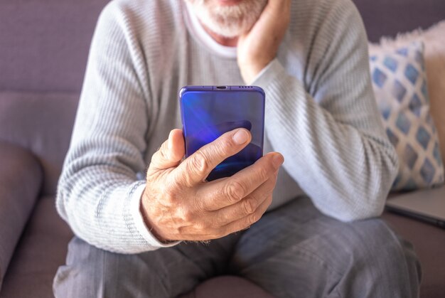 Hombre mayor sentado en el sofá en casa mediante teléfono móvil. Concepto de personas jubiladas de ocio