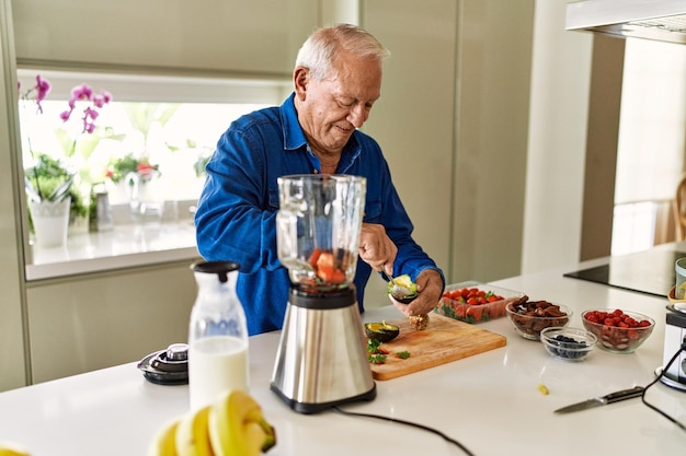 Hombre mayor sonriendo confiado cortando aguacate en la cocina