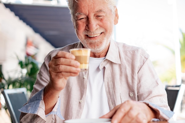 Hombre mayor sonriente sentado al aire libre en una mesa de café disfrutando de café con leche