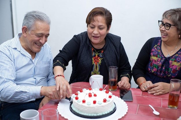 Foto un hombre mayor con sus amigos celebrando un cumpleaños cortando un pastel en una fiesta interior vieja